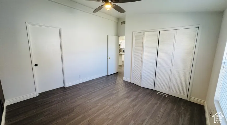 Vaulted ceilings featuring a central ceiling fan and light fixture, wood-finish flooring, and dual-panel closet doors with louvered detailing