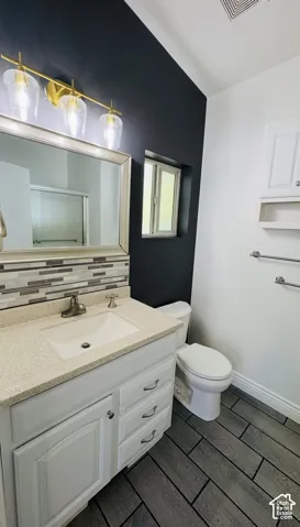 Bathroom vanity with stone-finish countertop, undermount sink, linear glass tile backsplash, three-light gold fixture, and gray rectangular floor tile