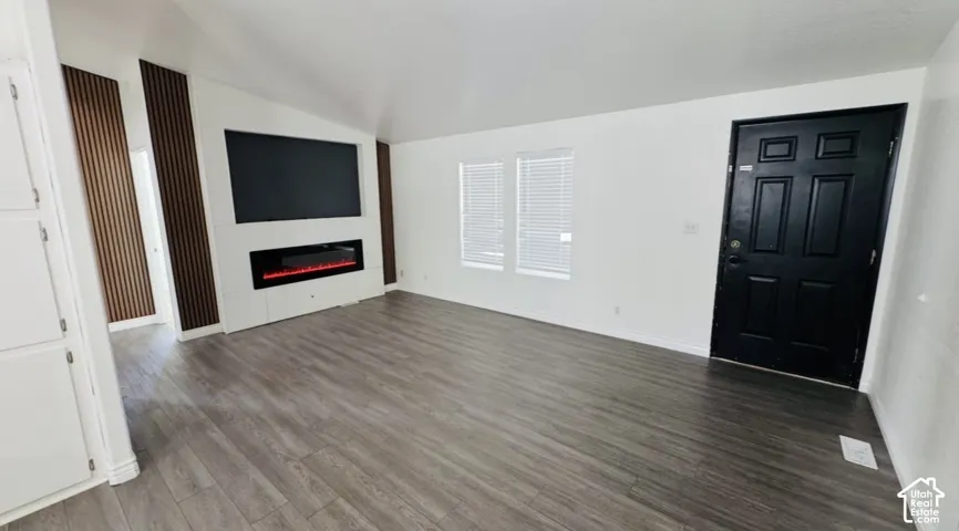 Living area featuring wood-finish flooring, a contemporary electric fireplace, vertical slat wood accent wall, and a six-panel exterior entry door
