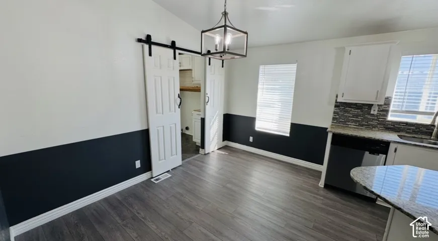 Wood-finish flooring, white cabinetry with stone-patterned countertops, decorative tile backsplash, white sliding barn doors with black hardware, and a metal-frame pendant light fixture