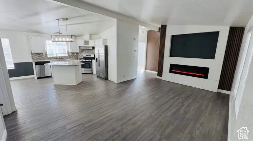 Kitchen featuring a center island, stainless steel appliances, and white cabinetry, accompanied by a living area with a built-in electric fireplace and decorative wood-finish wall panels