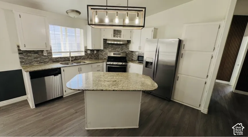 Kitchen featuring white cabinetry, stone-surface countertops, multi-toned tile backsplash, stainless steel appliances, and a central island with hanging pendant lighting