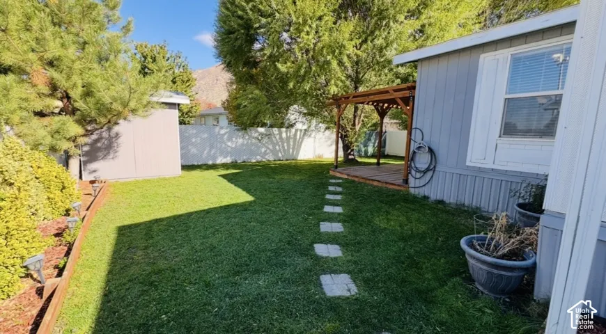 Backyard featuring a grass lawn, white vinyl fencing, a wood-frame pergola, stone paver pathway, and a detached storage structure