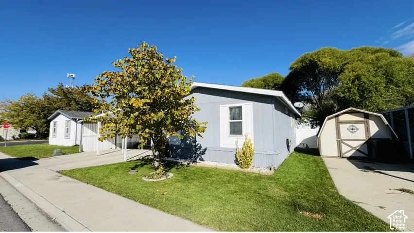 Exterior featuring light-toned vertical siding, attached carport, detached storage shed, and manicured lawn