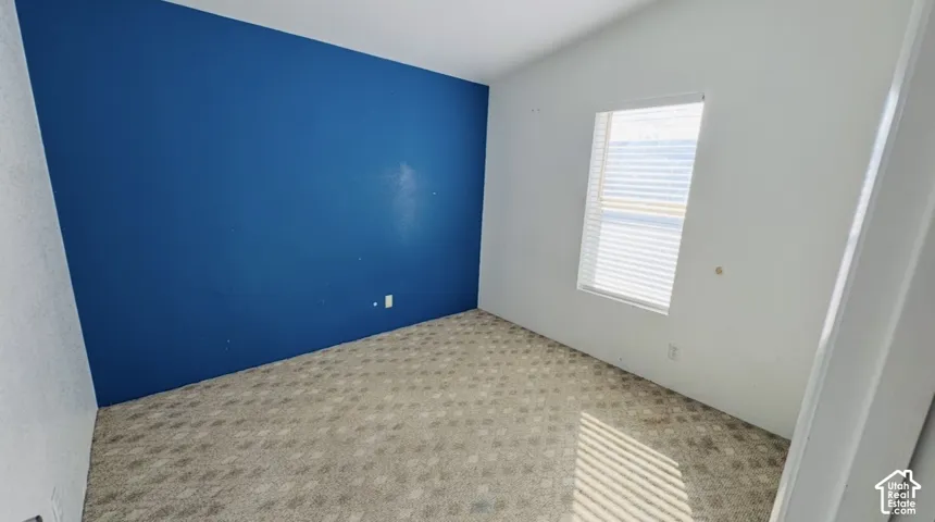 Room featuring a bold blue accent wall, neutral carpeting, and a single-hung window with horizontal blinds