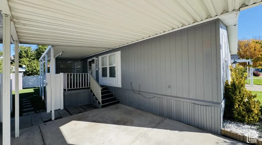 Covered carport featuring gray vertical siding, concrete pad, and an elevated porch with white railings and stairs