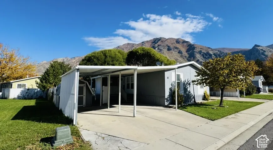 Single-story residence featuring a metal carport, concrete driveway, attached storage shed, and exterior mountain backdrop