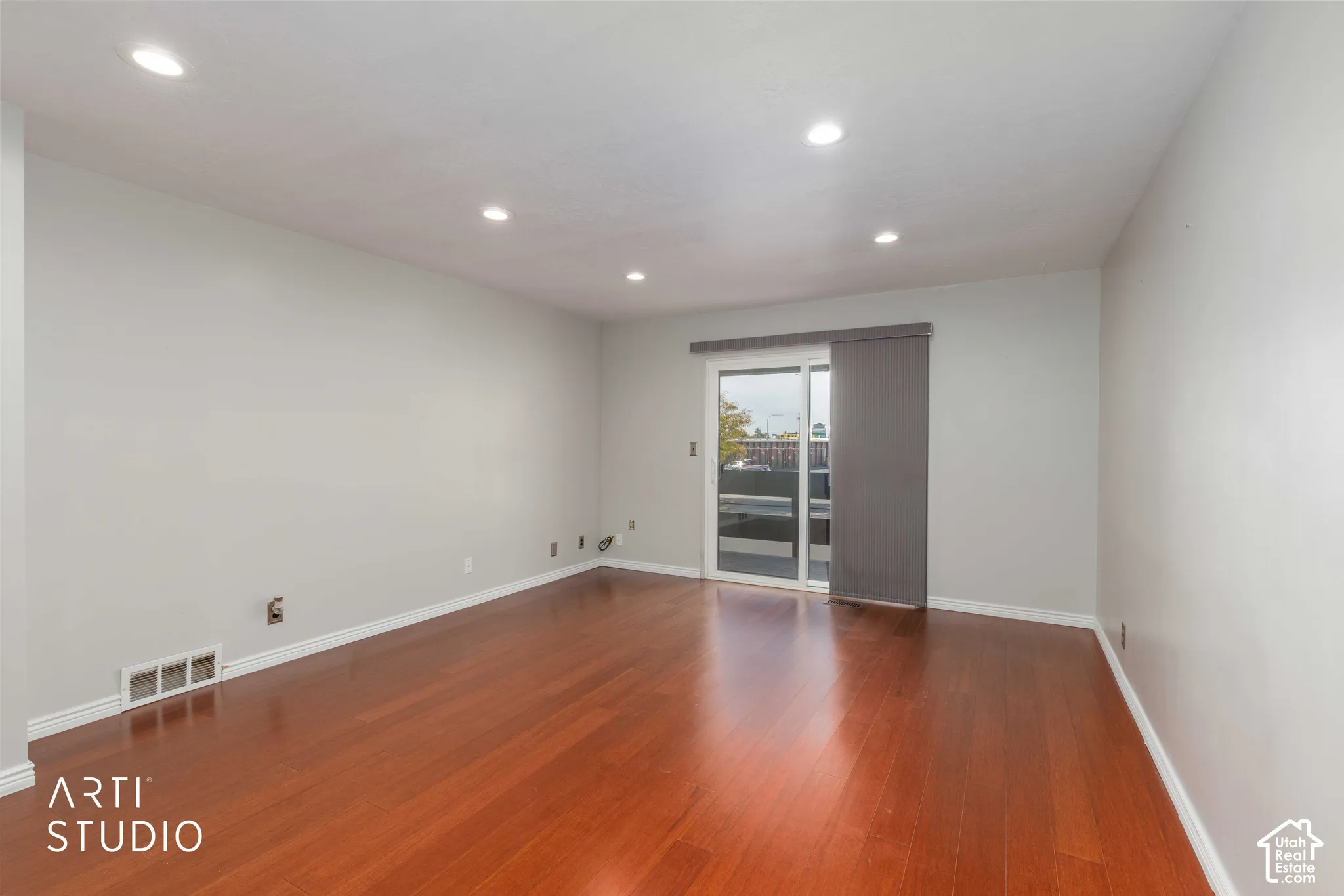 Open-concept room featuring wood-finish flooring, recessed lighting, and a sliding glass door with a panel track blind