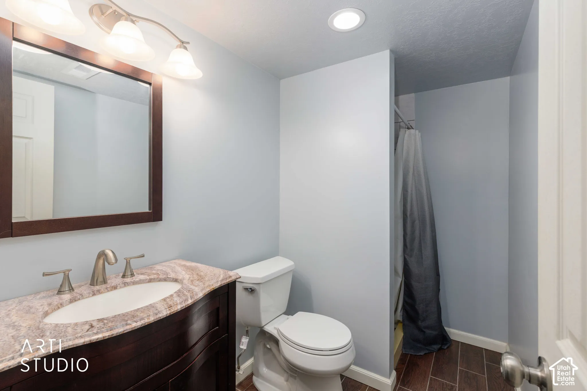 Dark wood-finish vanity with a stone-top vanity and undermount sink, framed wall mirror, polished metal fixture, and wood-finish flooring