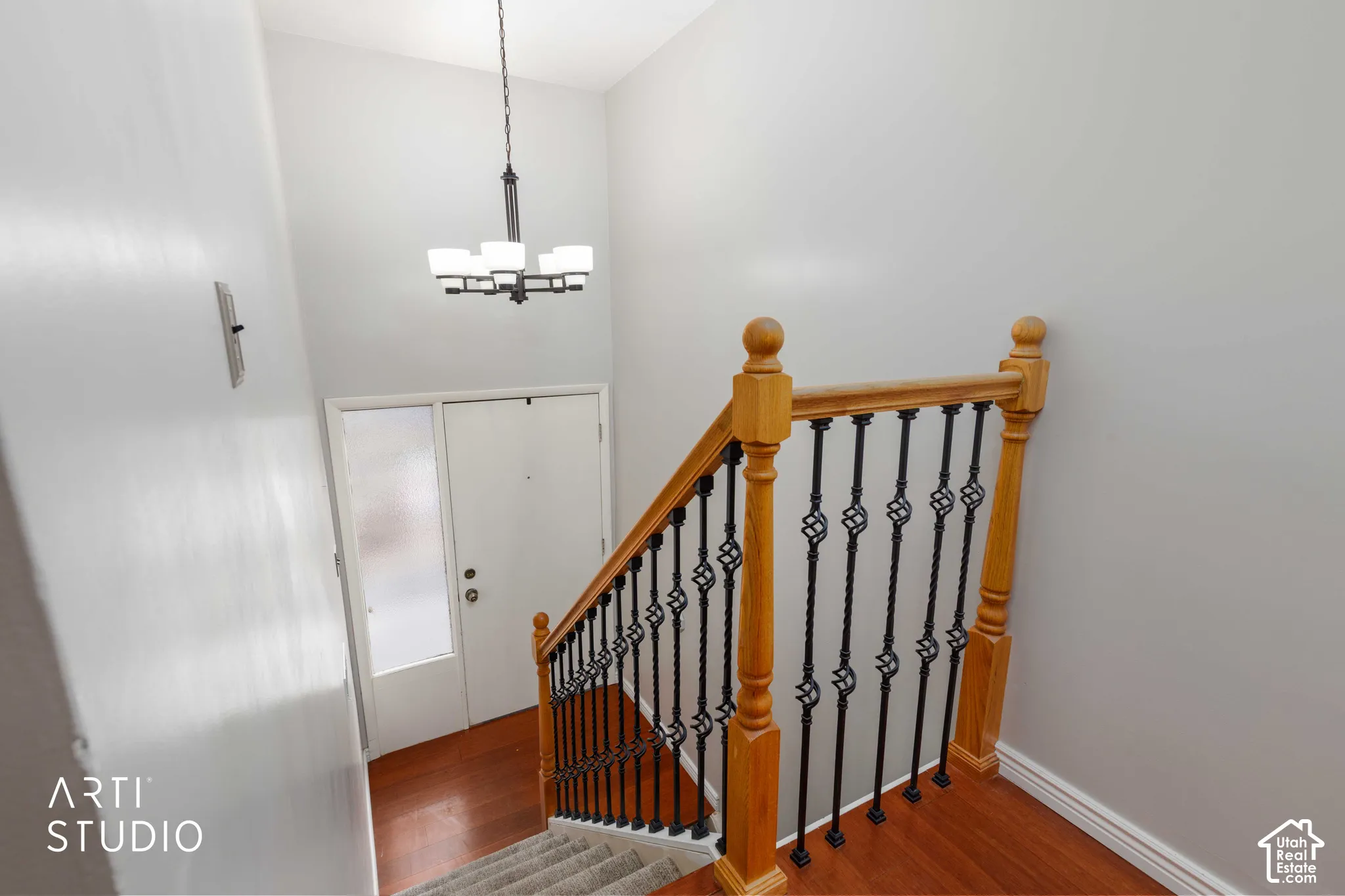 Entryway featuring a metal chandelier, front door with a glass sidelight, and a staircase with a wooden handrail and decorative metal balusters