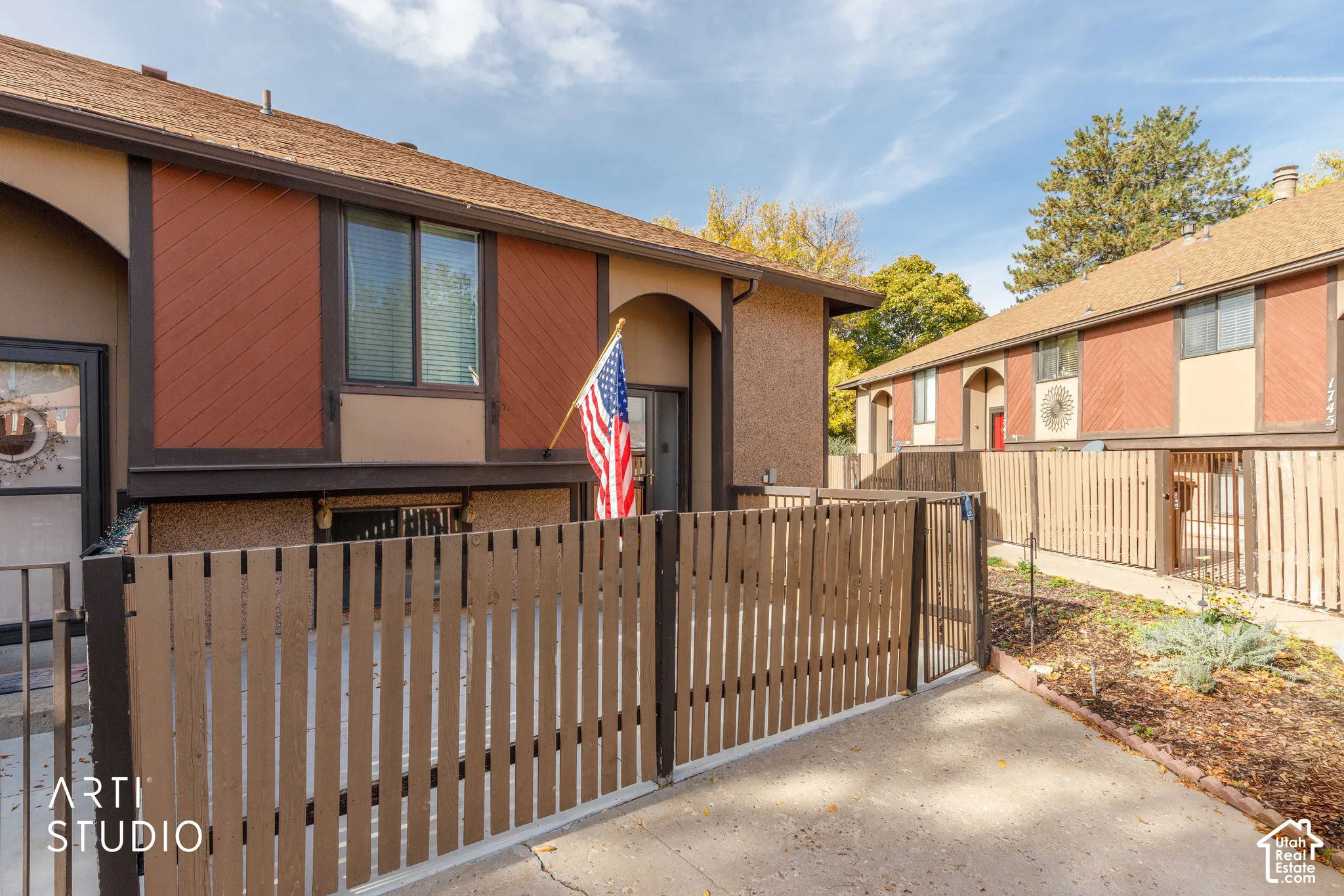 Exterior facade featuring diagonal wood-panel siding, arched entryways, and a private enclosed patio area with wood fencing
