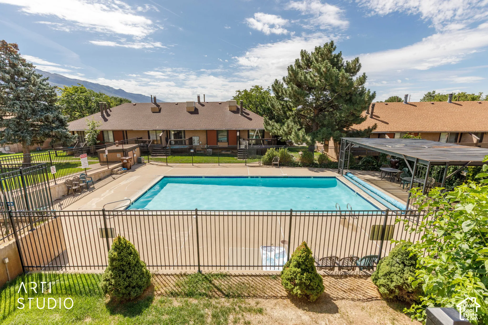 Outdoor swimming pool featuring a concrete deck, metal perimeter fencing, and a covered pavilion