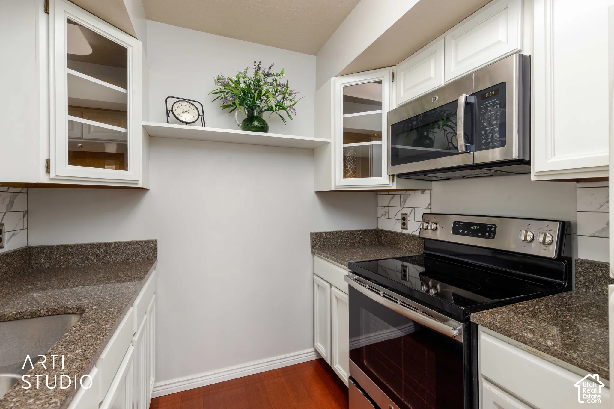 Kitchen featuring white cabinetry with glass-panel upper doors, stone-finish countertops, stainless steel appliances, and tile backsplash