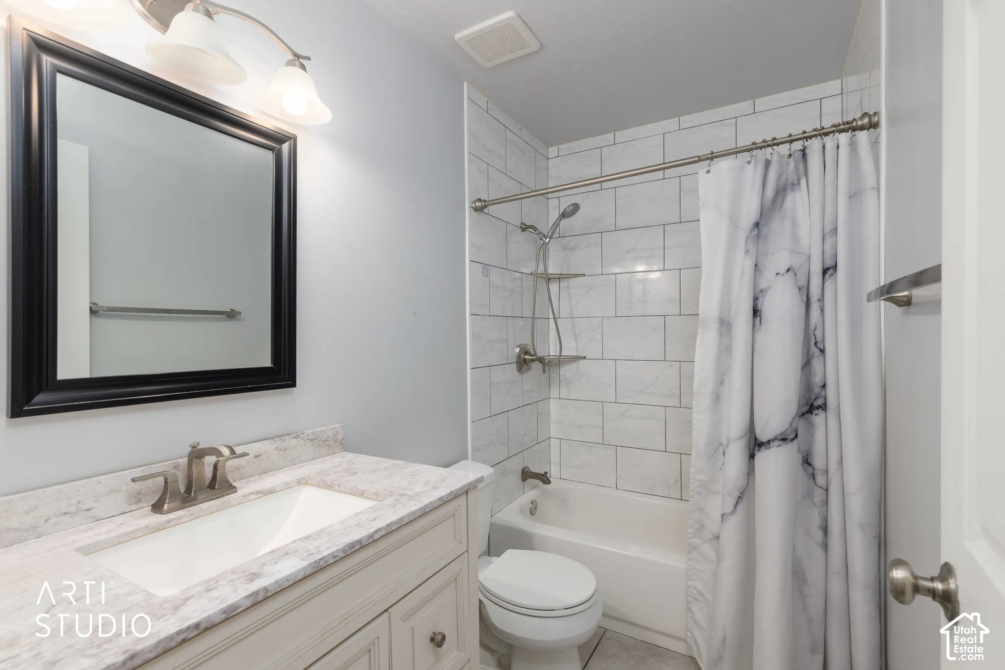 Bathroom featuring a vanity with a stone-finish countertop, undermount sink, framed wall mirror, and a tub-shower combination with floor-to-ceiling subway tile surround