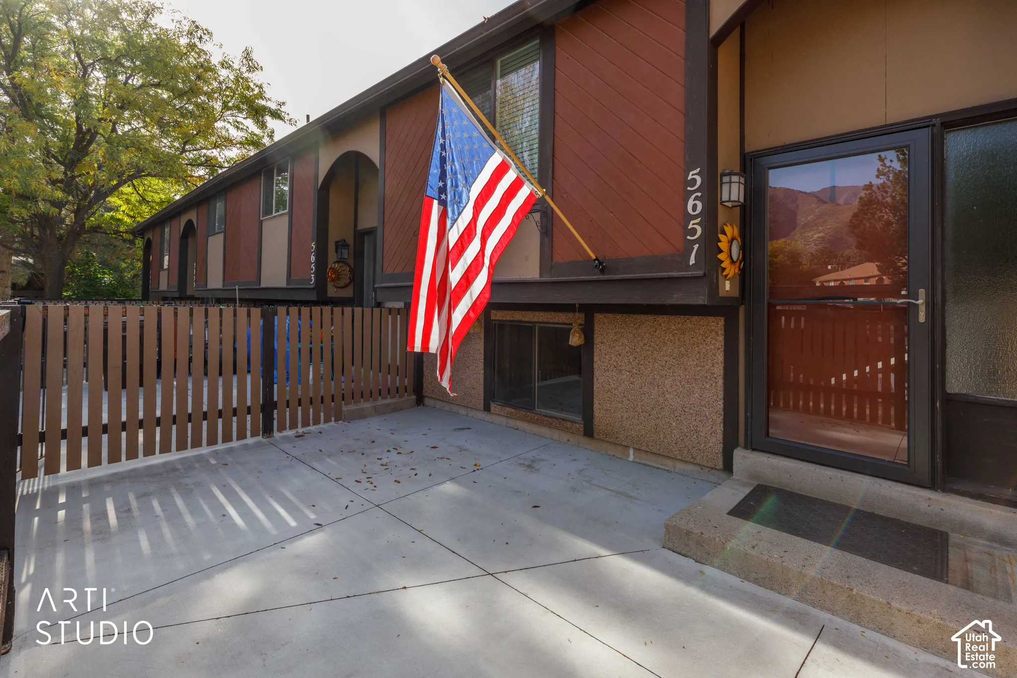 Concrete patio entrance featuring a metal picket privacy fence, textured masonry siding, dark-finish trim, and a glass-paneled storm door