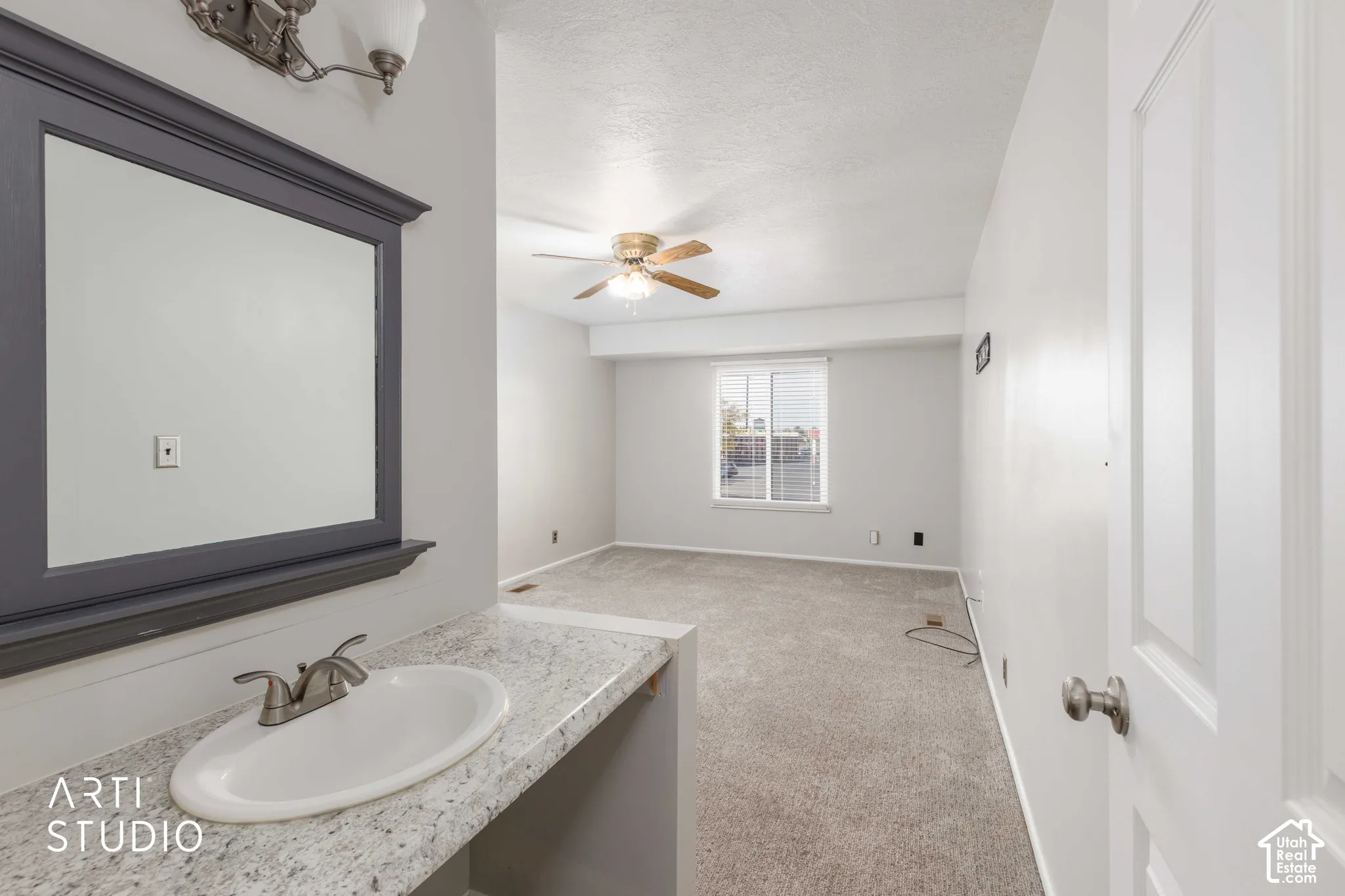 Vanity area featuring a stone-look countertop, integrated oval basin, and a framed wall-mounted mirror with an overhead light fixture, accompanied by carpeting and a ceiling fan