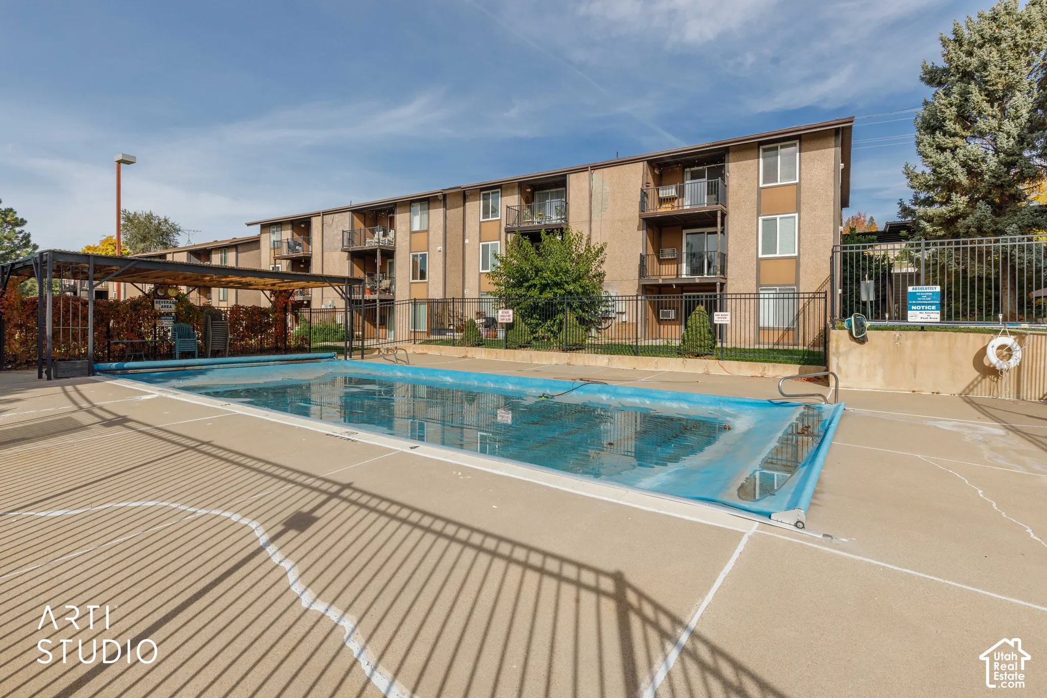 Swimming pool with concrete decking, pergola-covered seating area, and metal perimeter fencing