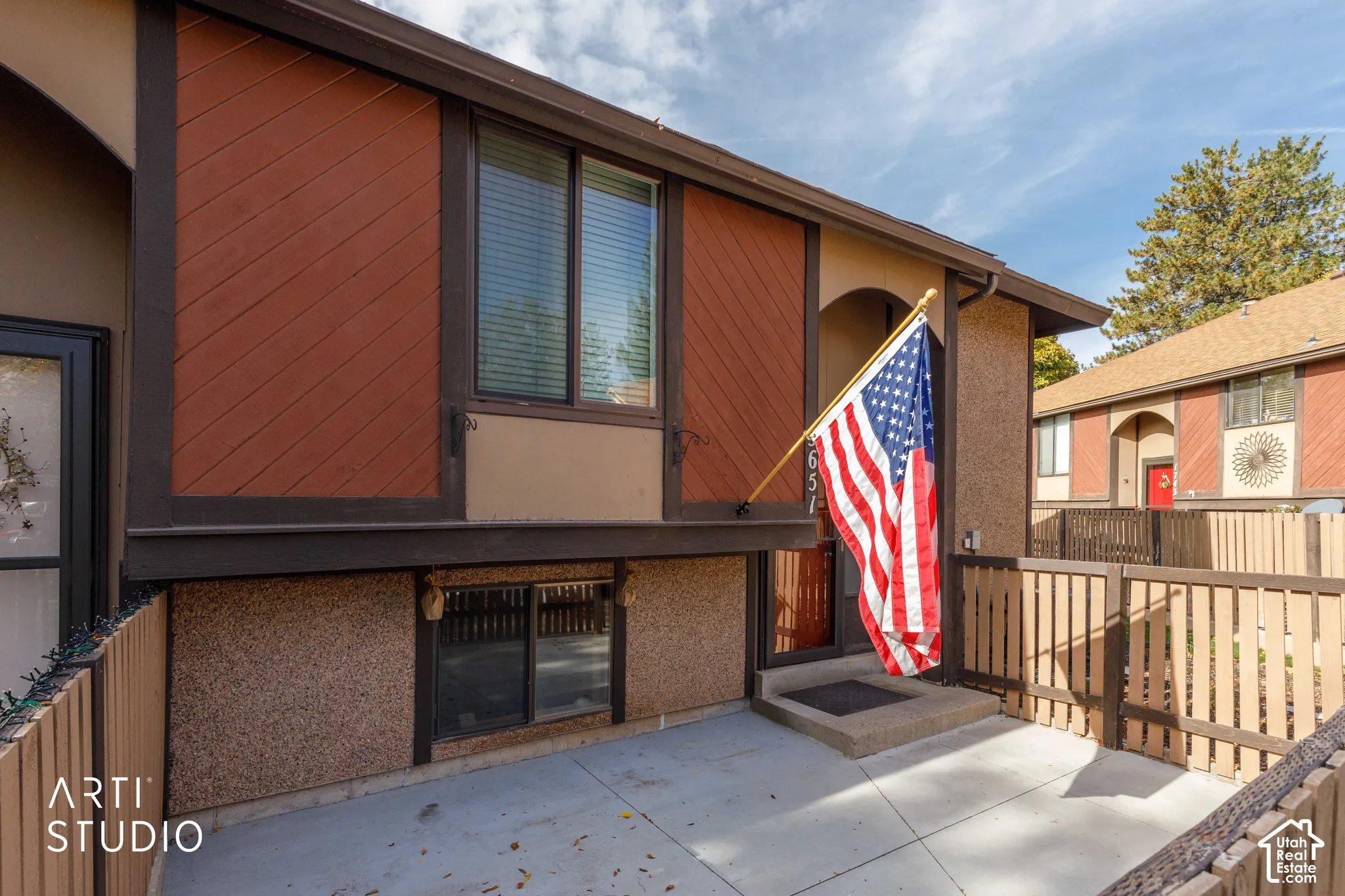 Exterior facade featuring stucco siding, diagonal wood-panel accents, a concrete patio, and attached wood privacy fencing