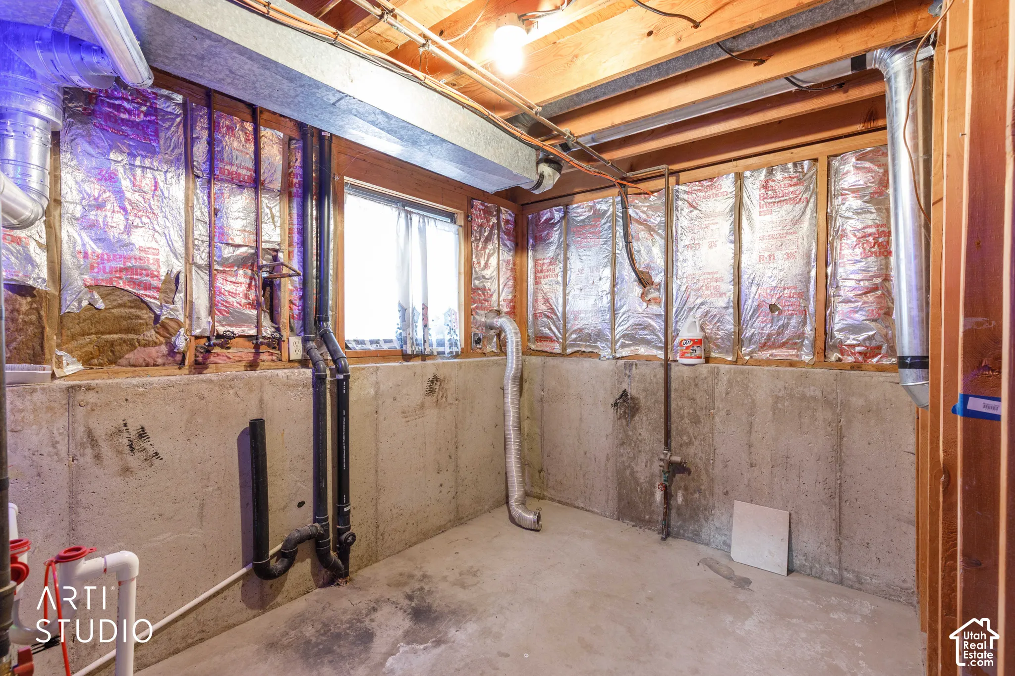 Unfinished space with exposed wood joists, poured concrete walls, and visible utility plumbing