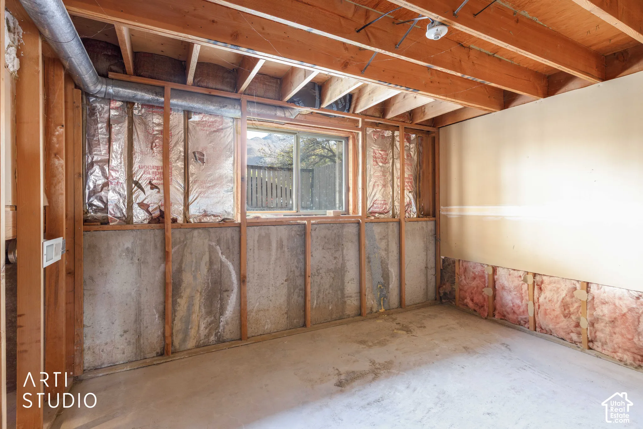 Unfinished interior space featuring exposed wood framing, concrete foundation walls, fiberglass insulation, and a single-pane slider window
