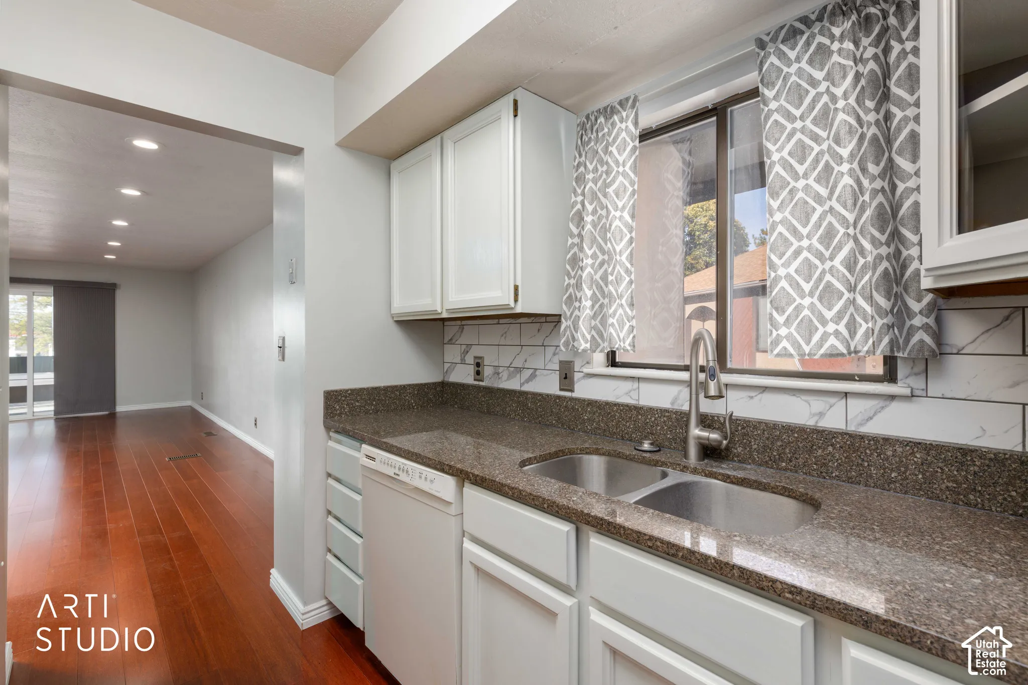 Kitchen featuring white cabinetry, solid-surface countertops, subway tile backsplash, and stainless steel dual-basin sink with pull-down faucet