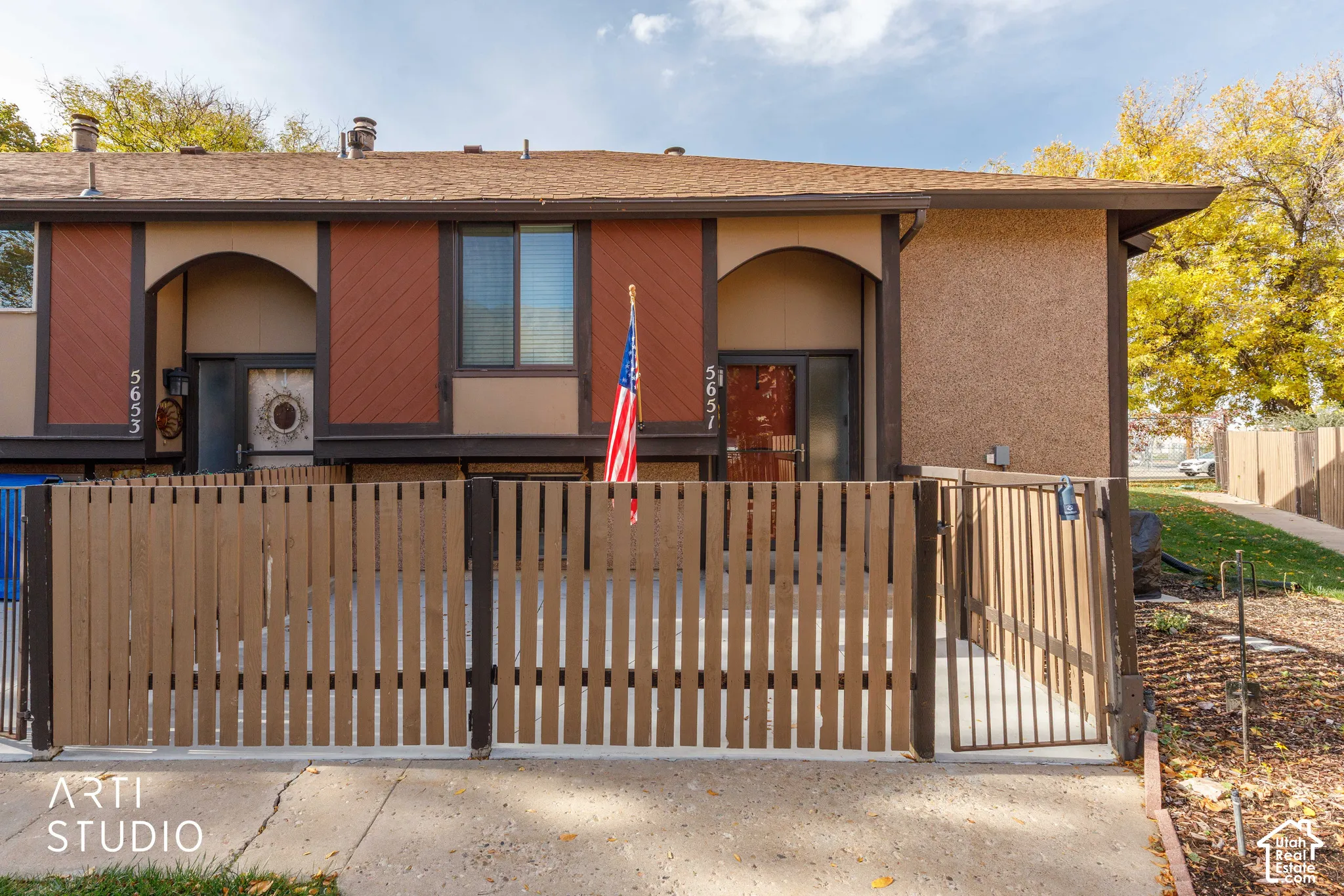 Exterior facade featuring textured stucco and diagonal wood-paneled siding, complemented by an enclosed patio area with vertical wood-slat fencing and arched entryways