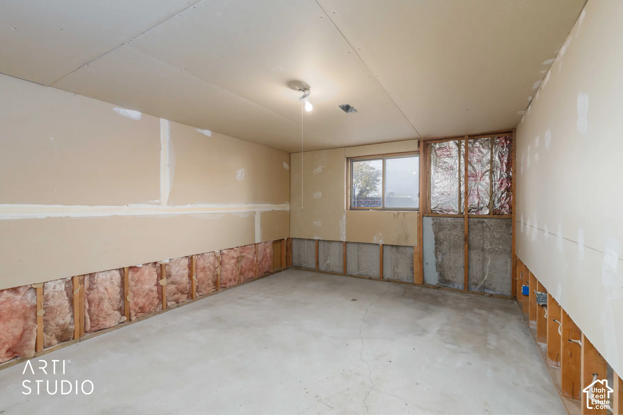 Unfinished space featuring exposed stud framing, fiberglass batt insulation, concrete flooring, and a single-pane sliding window