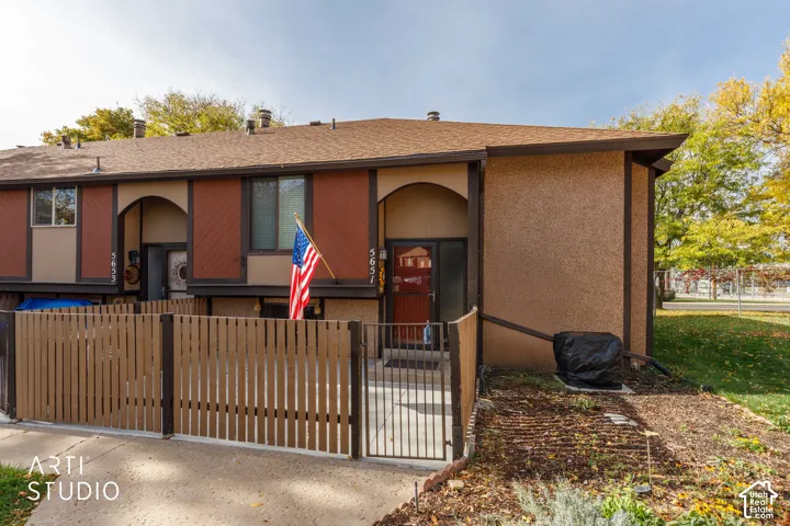 Multi-unit exterior featuring textured stucco siding, decorative wood-panel accents, arched entryway, and private fenced patio area