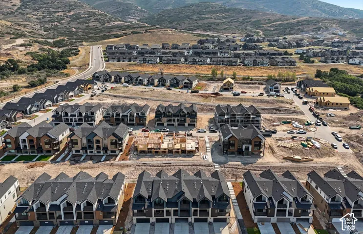 Aerial perspective of a multi-unit residential community featuring staggered rooflines, attached garage access, paved roadways, and mountain backdrop