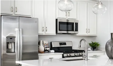 Kitchen featuring white shaker-style cabinetry, stainless steel appliances, quartz countertops, a stainless steel undermount sink with a gooseneck faucet, and glass pendant lighting