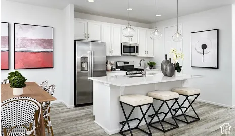 Kitchen featuring white shaker-style cabinetry, a central island with a solid surface countertop, stainless steel appliances, wood-finish flooring, and glass pendant lighting