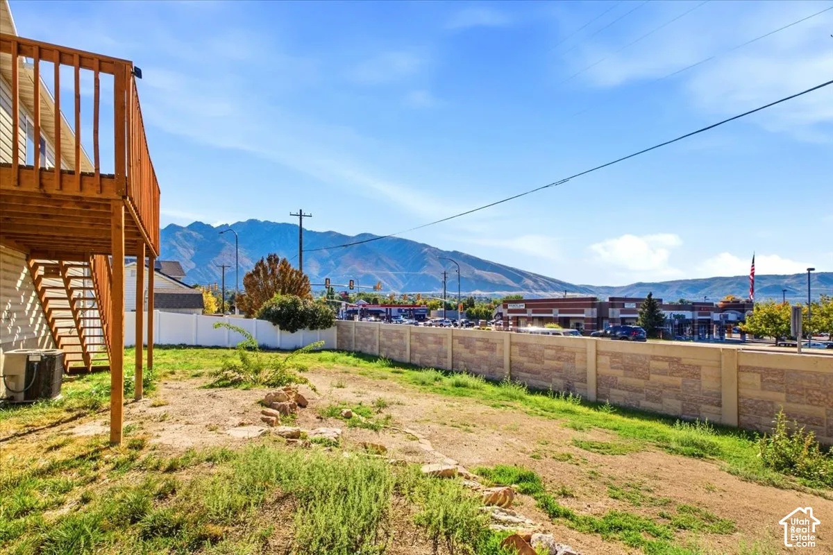 Rear outdoor space featuring a raised wooden deck with staircase, a perimeter masonry wall, and mountain backdrop