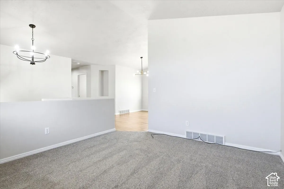 Interior space featuring neutral wall-to-wall carpeting, wood-finish flooring, two modern multi-light chandeliers, and a wall niche