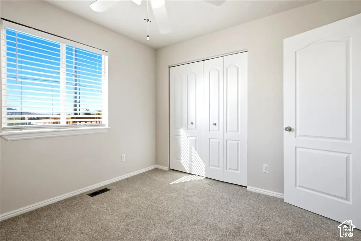 Neutral wall coloring, carpeted flooring, white multi-panel bi-fold closet doors, white raised-panel interior door, and a white ceiling-mounted fan with integrated lighting