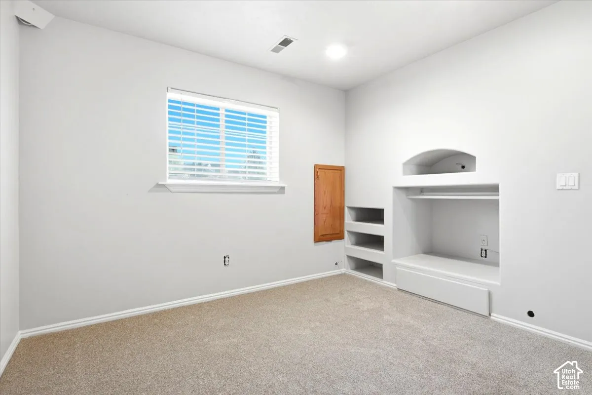 Neutral-toned room featuring wall-to-wall carpeting, an inset media niche with an arched decorative header, built-in shelving, and a wood-panel access door
