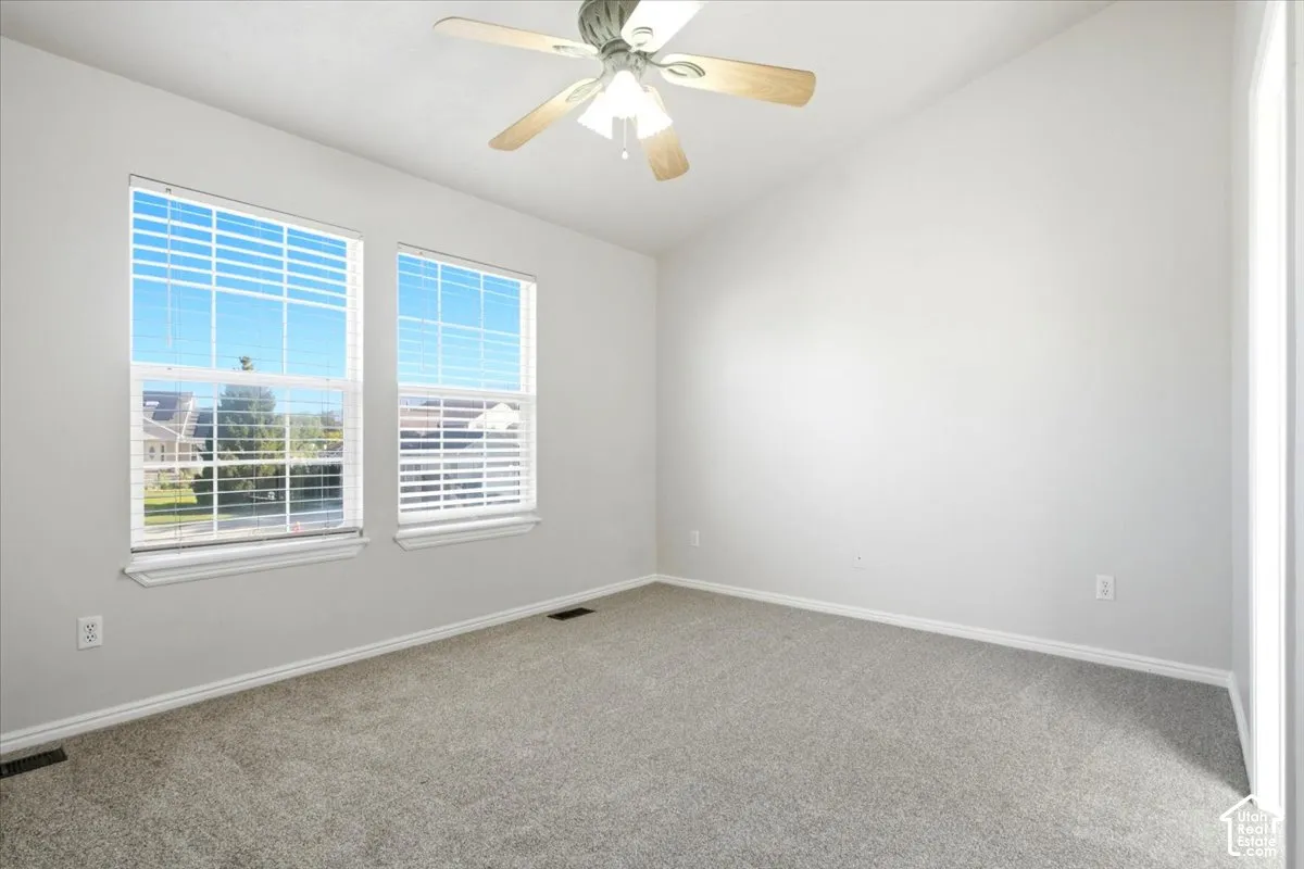 Vaulted ceiling, neutral wall tones, dual double-hung windows, and a ceiling-mounted light fixture with a fan