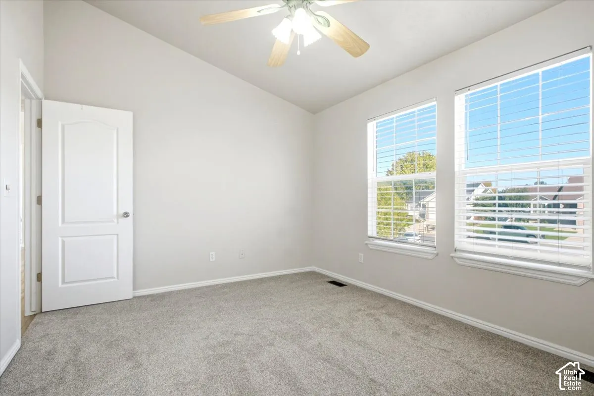 Vaulted ceiling, neutral wall tones, wall-to-wall carpeting, dual windows, and a ceiling fan with integrated lighting