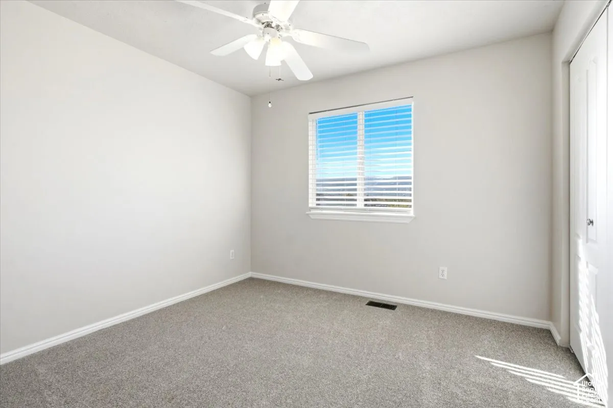 Neutral-toned carpeted flooring, white interior walls, ceiling fan with integrated lighting, and dual-panel closet doors