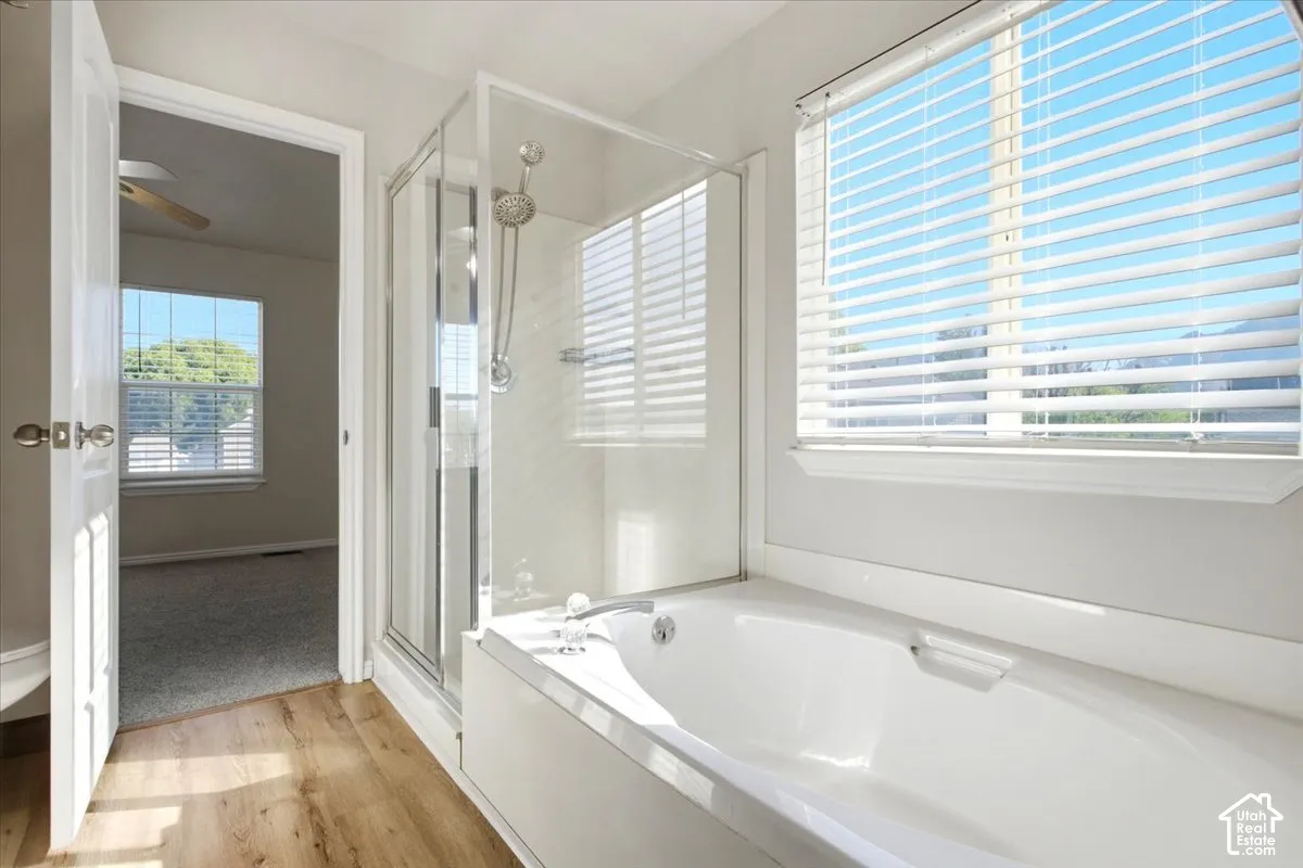 Bathroom featuring a glass-enclosed shower, deep soaking tub with polished chrome fixtures, wood-finish flooring, and a window with white horizontal blinds