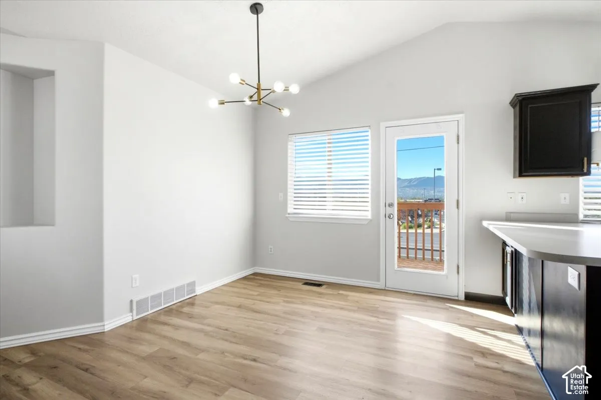 Vaulted ceiling, wood-finish flooring, modern multi-arm chandelier, built-in wall niche, and exterior door with glass insert