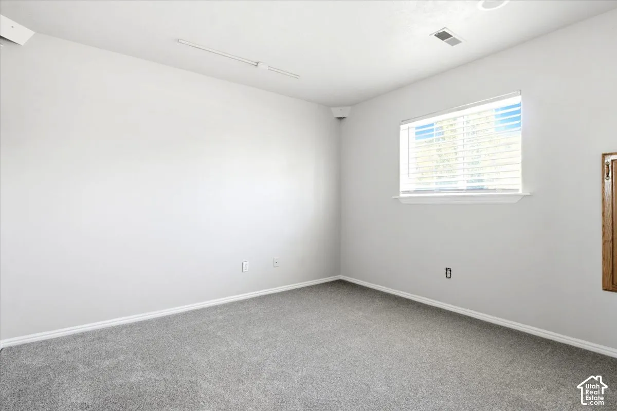 Neutral-toned carpeted flooring, white wall finish, and a rectangular window equipped with horizontal slat blinds