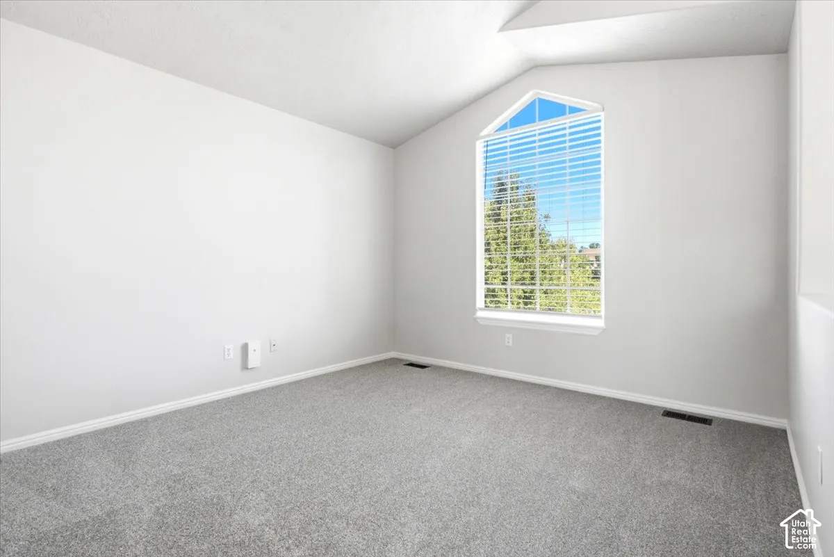 Neutral carpeted flooring, vaulted ceilings, and a large gable-style window