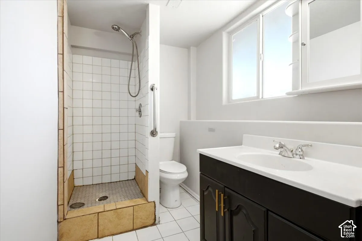 Bathroom featuring a walk-in shower with white tile surround, dark-finish vanity cabinet with a light-tone countertop, built-in medicine cabinet, and ceramic tile flooring