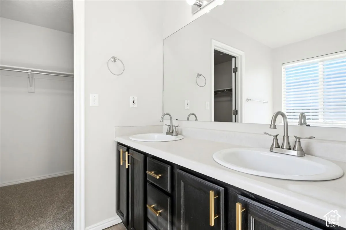 Dual-sink vanity with matte black cabinetry, gold-tone hardware, light-toned solid surface countertop, and full-width vanity mirror