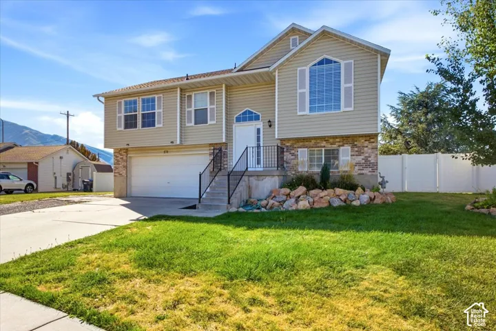 Multi-level exterior featuring vinyl siding, decorative stone masonry, attached two-car garage, arched accent window, and rock landscaping