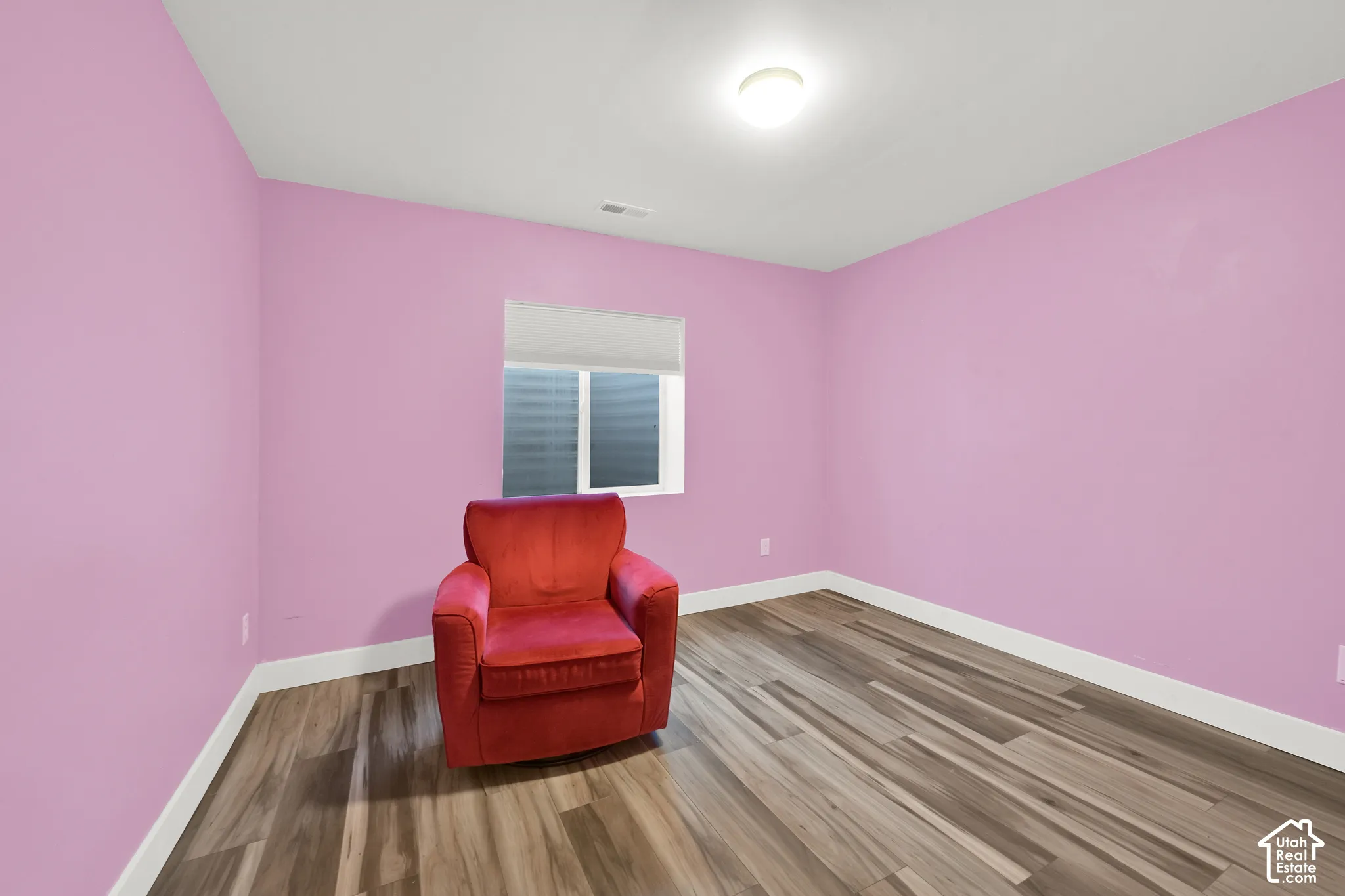 Room featuring wood-finish flooring, a recessed window with a roll-up shade, and a ceiling-mounted light fixture