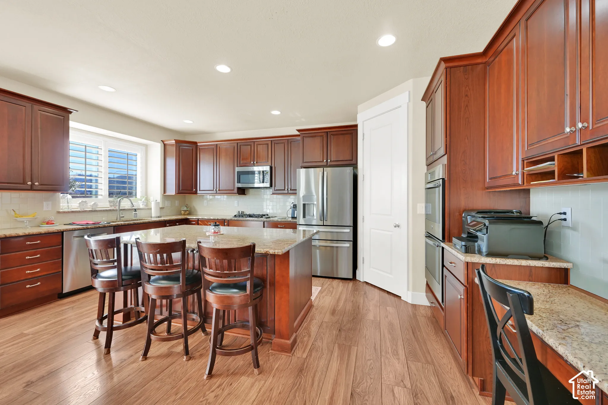 Kitchen featuring wood cabinetry, stone-surface countertops, stainless steel appliances including a double wall oven, central island, and wood-finish flooring