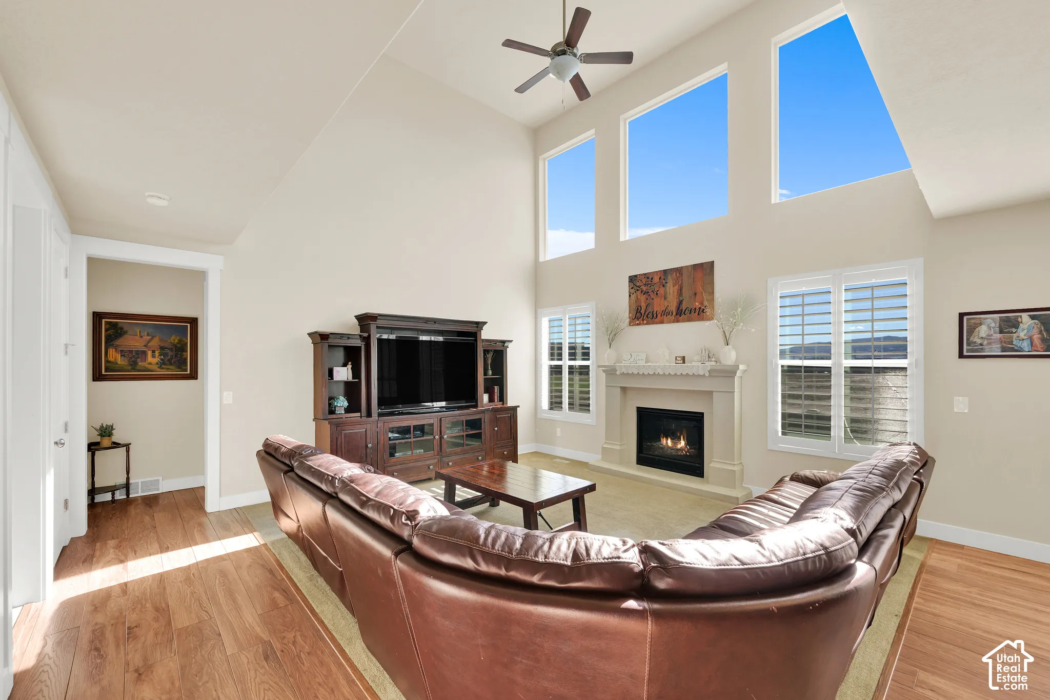 Vaulted ceilings with large windows, wood-finish flooring, fireplace with stone-finish surround, and plantation shutters
