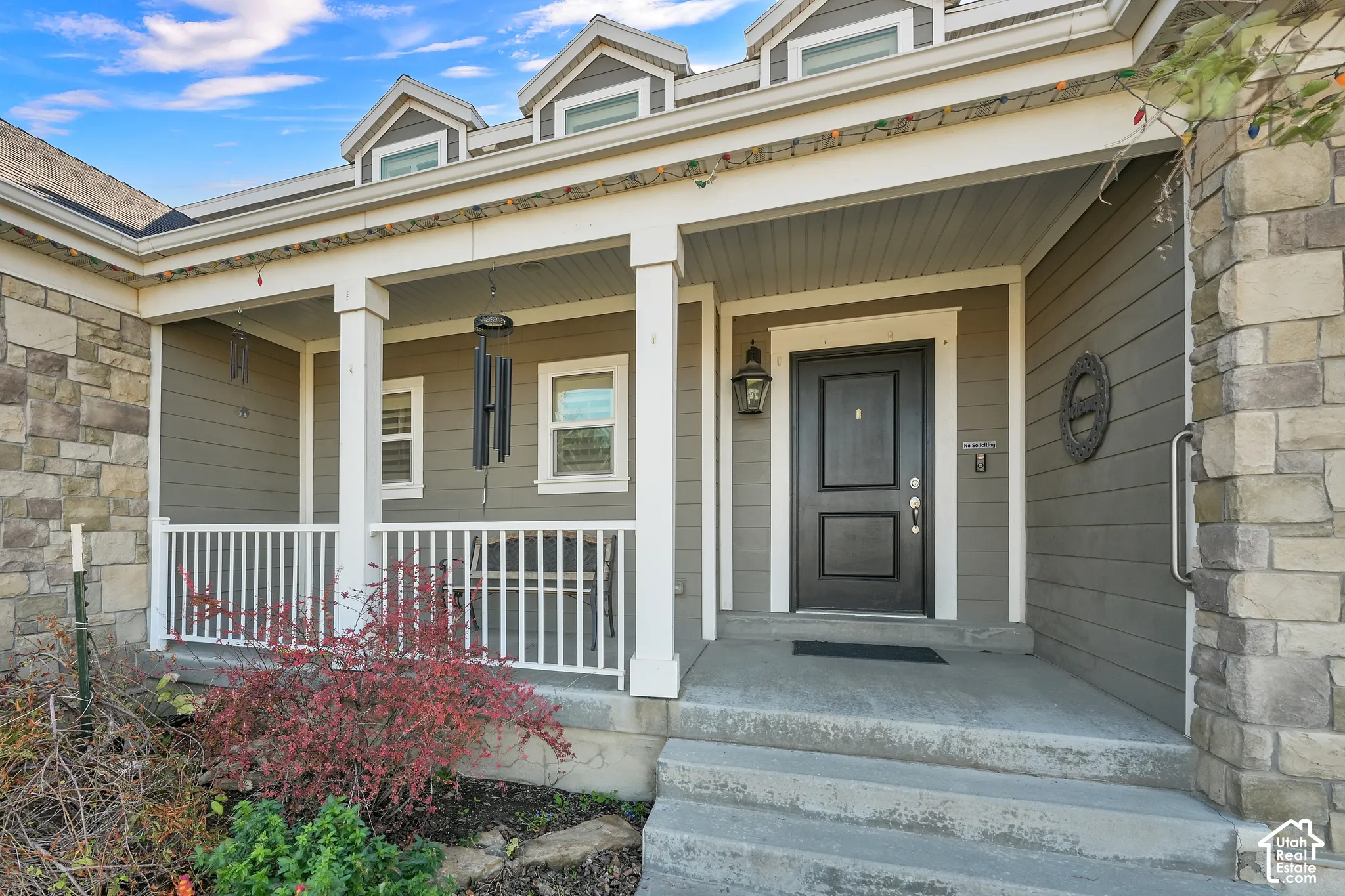 Covered front porch featuring stacked stone accents, horizontal lap siding, white wooden railings, and three roof dormers