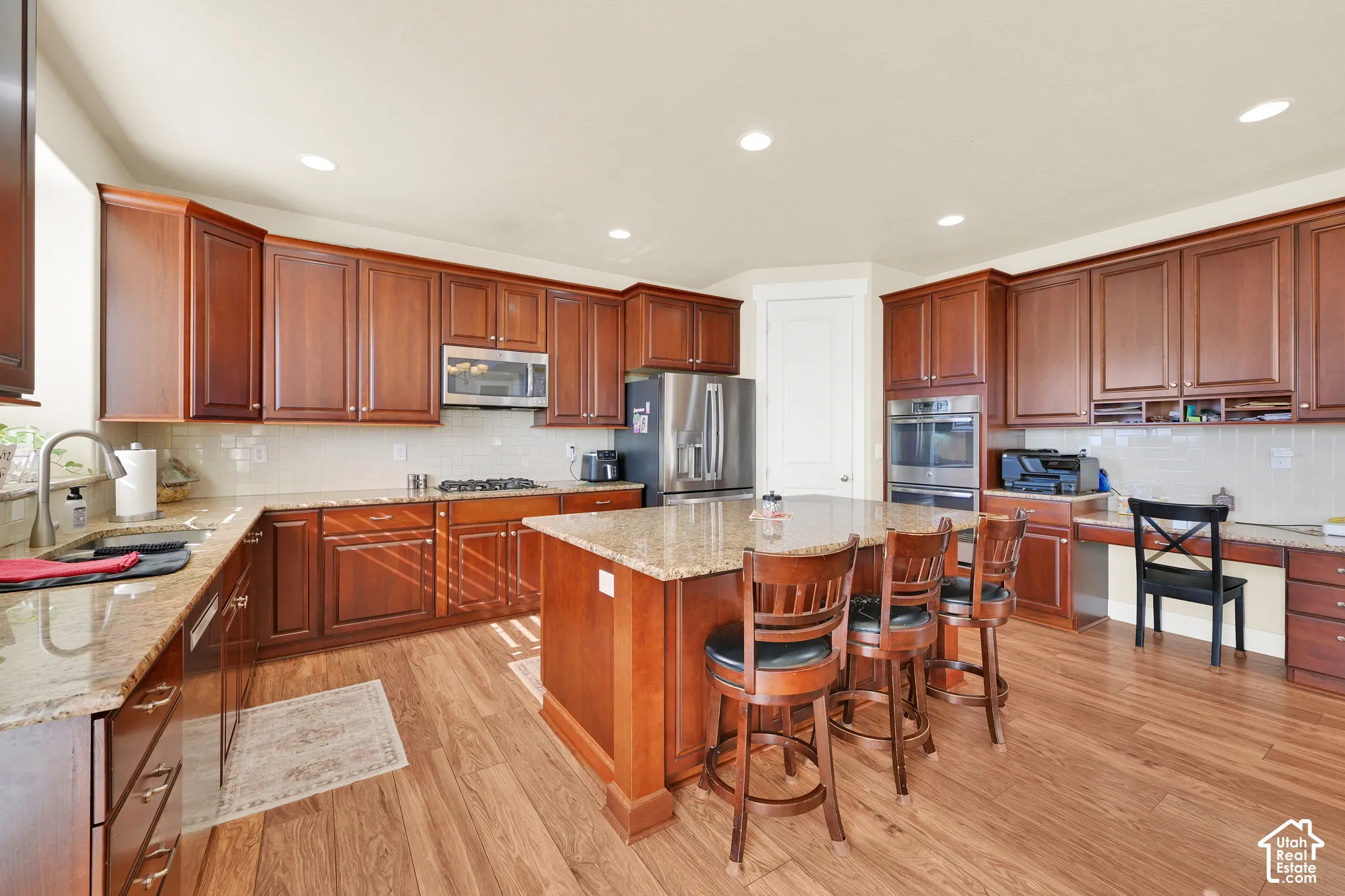 Kitchen featuring wood cabinetry, stone countertops, stainless steel appliances, a center island with bar seating, and wood-finish flooring